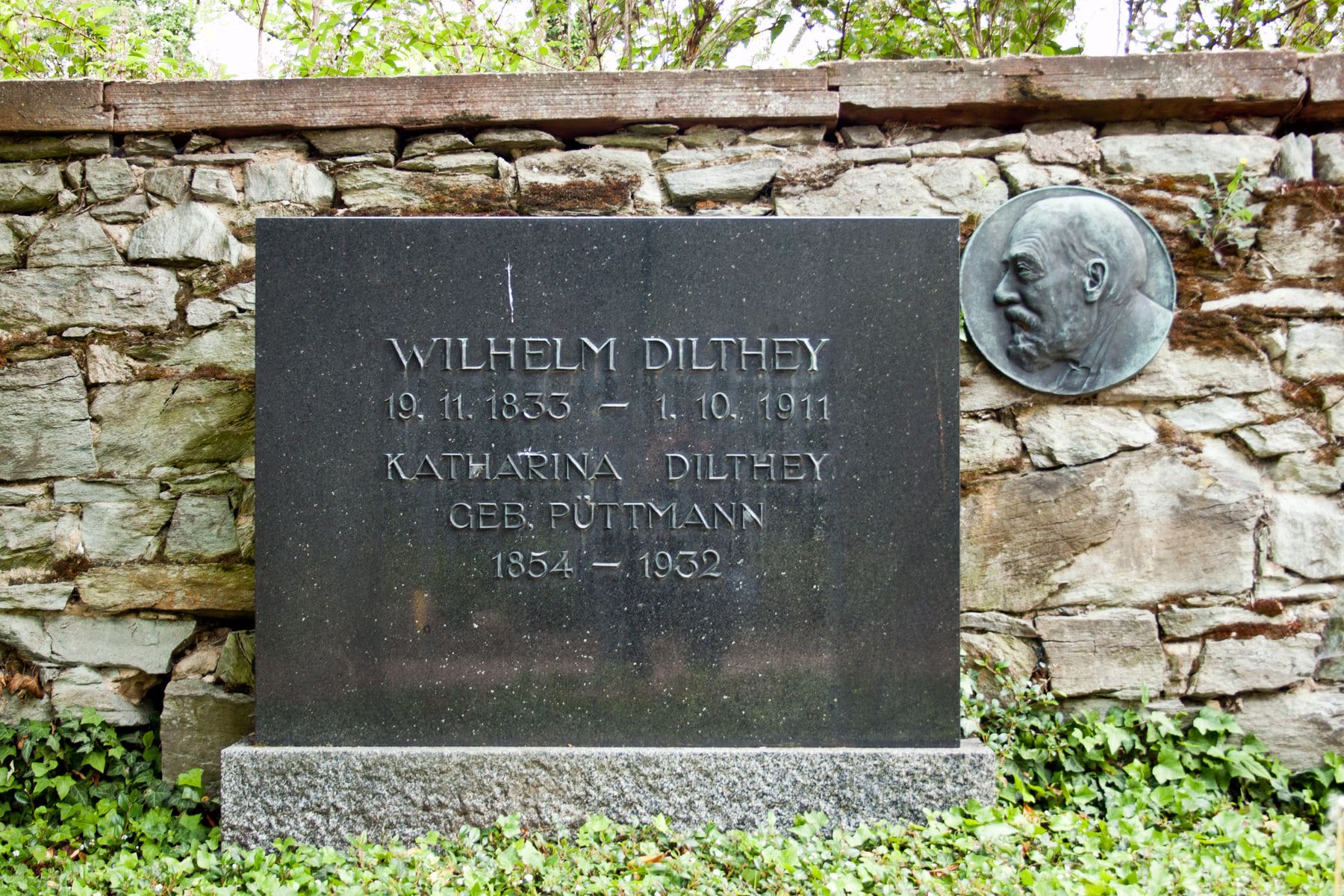 Nahaufnahme der schwarzen Namenstafel und des runden Porträtreliefs am Grab von Wilhelm und Katharina Dilthey auf Friedhof Biebrich